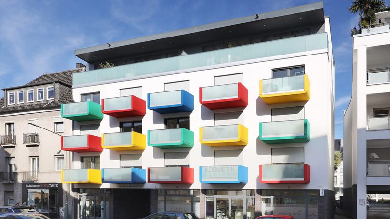 Mehrstöckiges Wohngebäude mit farbigen, kubischen Balkonen in Rot, Blau, Gelb und Grün
