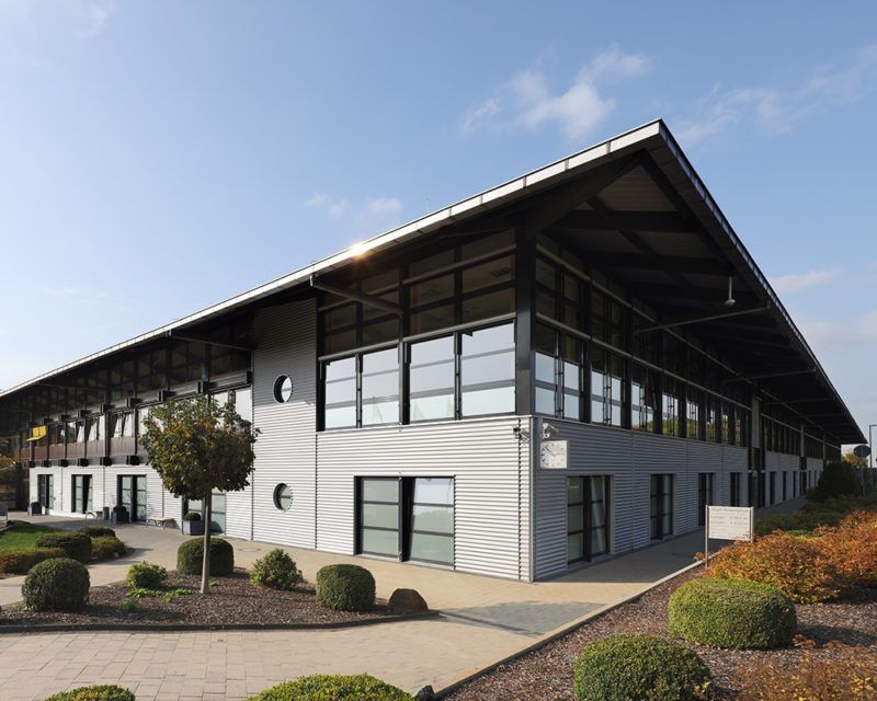Modernes zweistöckiges Bürogebäude mit großem Vordach und rechteckigen Fenstern in gepflegter Gartenanlage