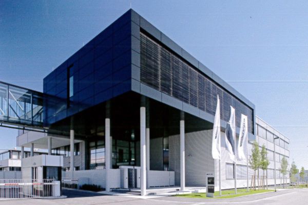 Modernes Bürogebäude mit großem, überdachtem Eingangsbereich, Glasfassade und drei Fahnenmasten davor