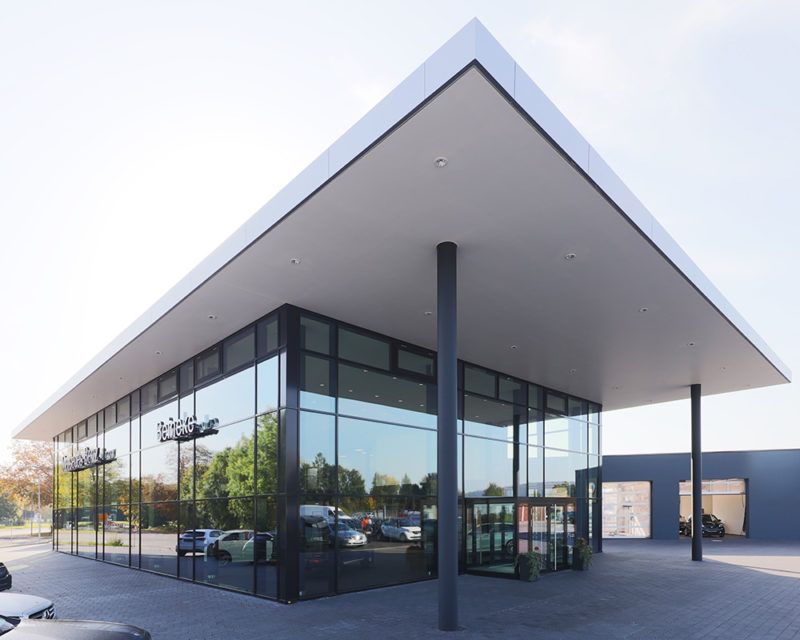 Modernes Gebäude mit großer Glasfassade und flachem, überstehendem Dach auf grauem Boden