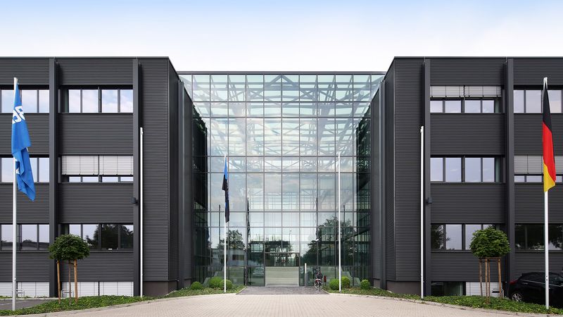 Moderne Bürogebäudefassade mit großem Glasportal und Flaggen vor dem Eingang