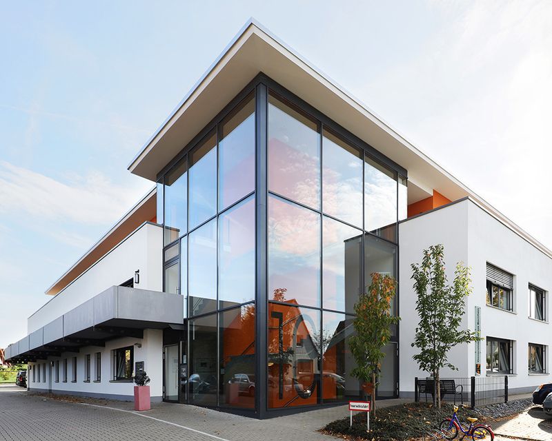 Modernes zweigeschossiges Gebäude mit großer Glasfassade und Flachdach, umgeben von Bäumen und einem Fahrrad