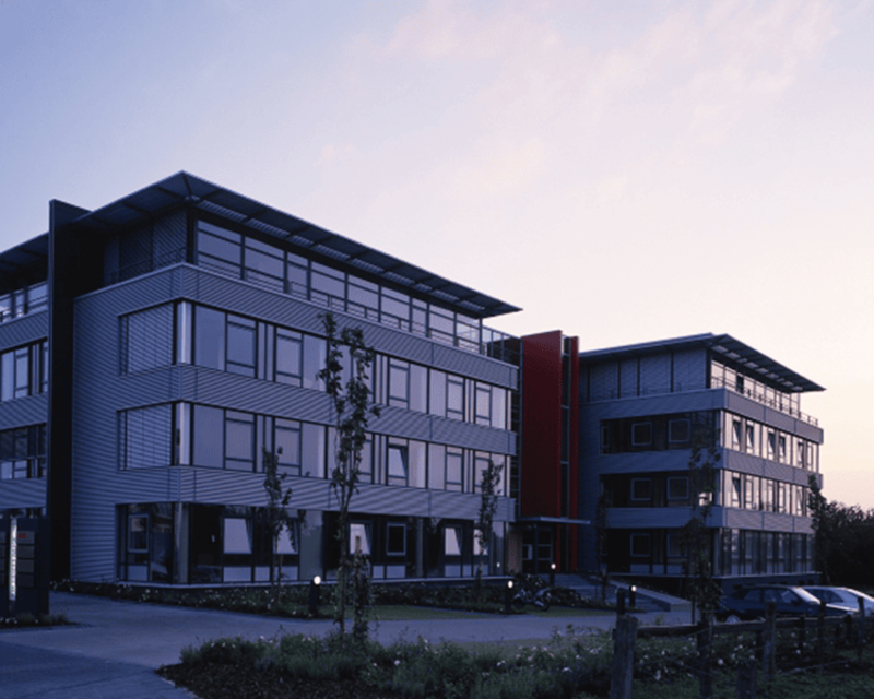 Zwei moderne Bürogebäude mit großen Fenstern und Flachdächern bei Dämmerung