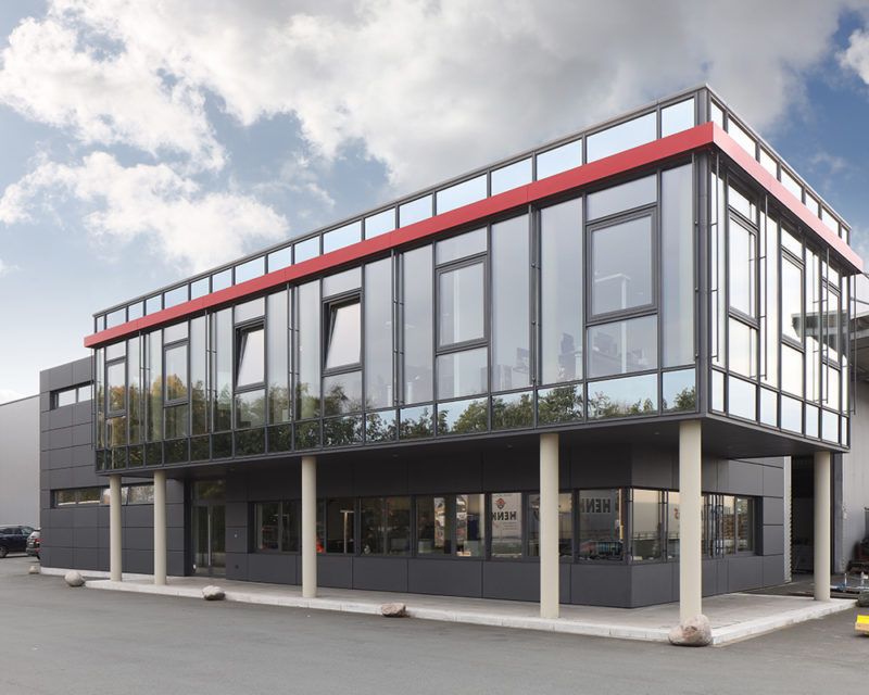 Modernes zweigeschossiges Bürogebäude mit großer Glasfassade und roten Akzenten auf der oberen Etage